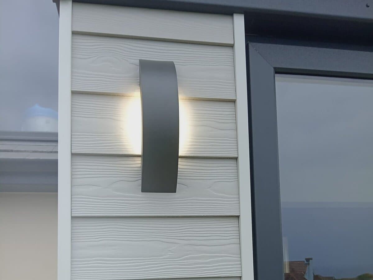 Modern outdoor wall light fitted on white cladding beside a glazed door